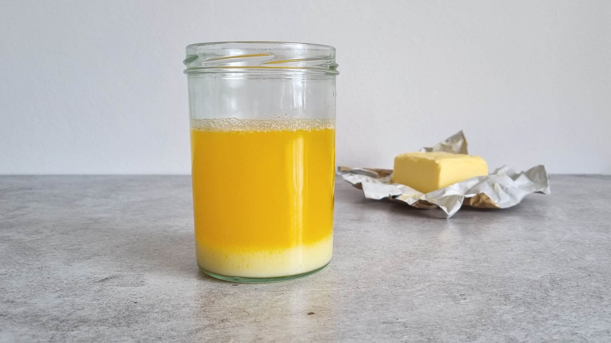 Melted butter in a glass. The butter has separated into three layers, a very light yellow layer at the bottom, a thicker layer of deep yellow and a thin white layer on top.