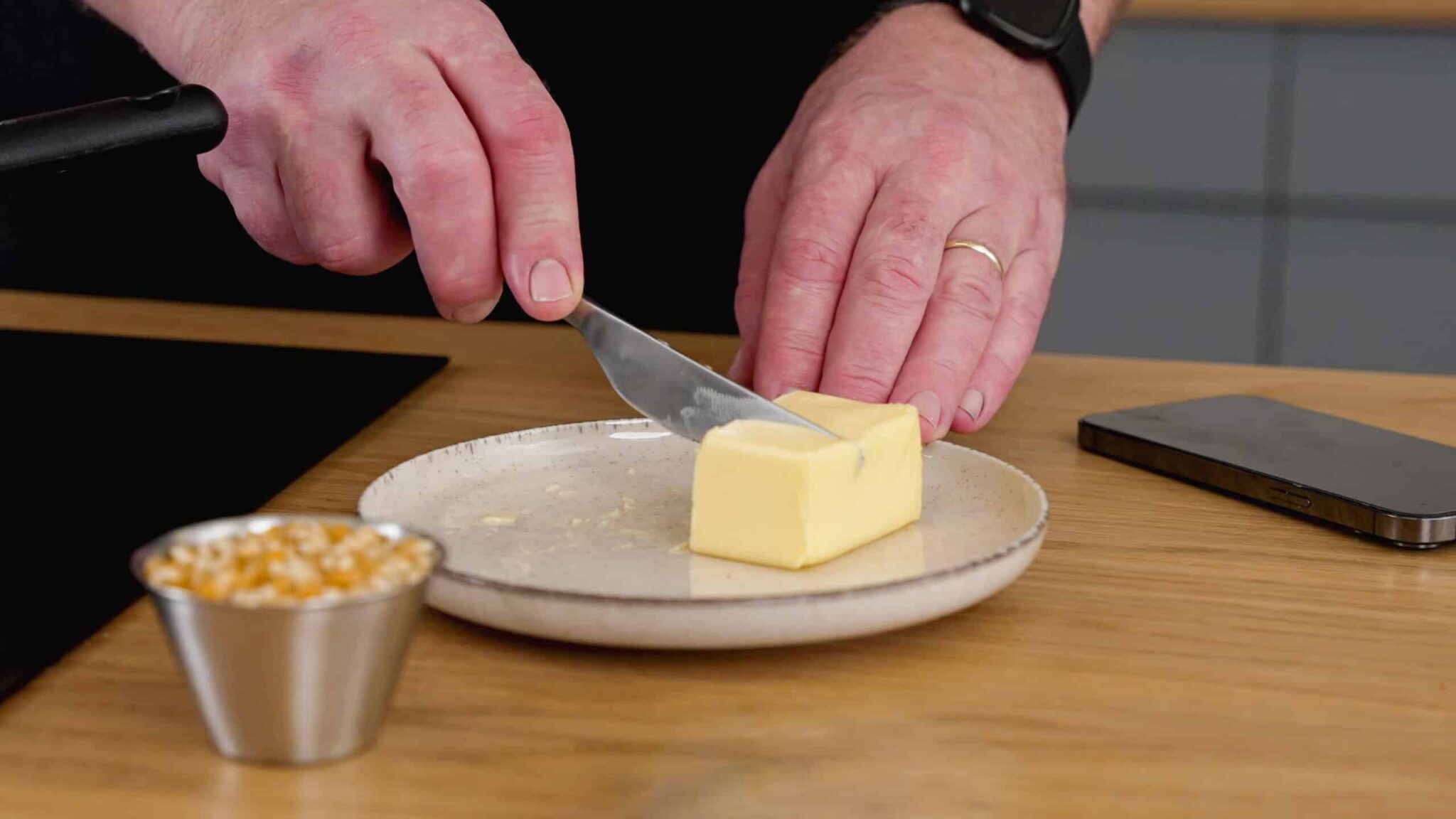 Smør der ligger på en tallerken ved siden af et decilitermål med popcornsmajs.